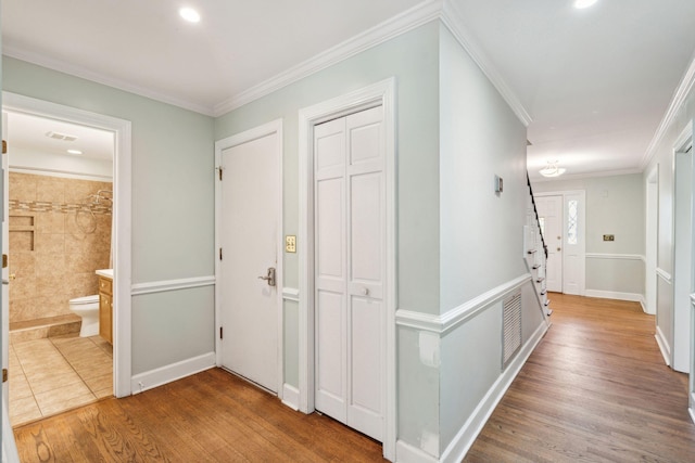 corridor with ornamental molding, visible vents, baseboards, and wood finished floors