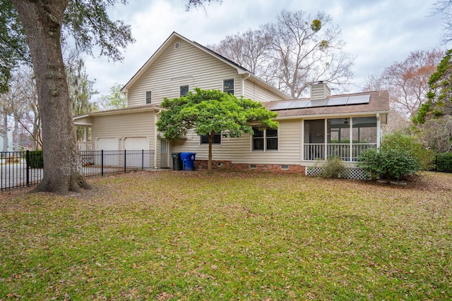 rear view of property featuring a chimney, a lawn, a sunroom, roof mounted solar panels, and fence