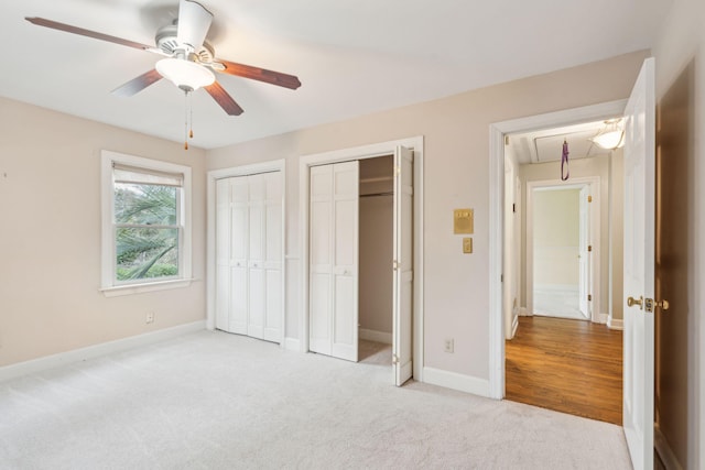 unfurnished bedroom featuring two closets, light colored carpet, attic access, ceiling fan, and baseboards