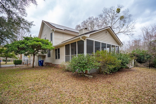 view of property exterior featuring a sunroom, a chimney, fence, and solar panels