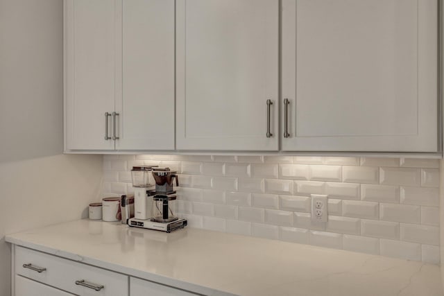 interior space featuring white cabinets, backsplash, and light stone countertops