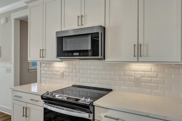 kitchen with white cabinets, light stone countertops, stainless steel appliances, and backsplash