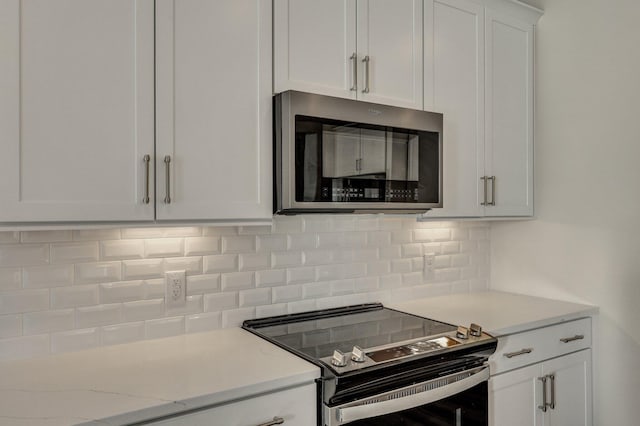 kitchen featuring appliances with stainless steel finishes, white cabinetry, light stone counters, and tasteful backsplash