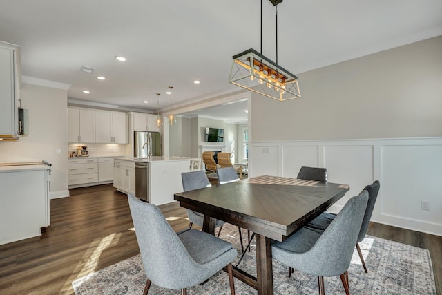 dining space featuring wainscoting, dark wood-style flooring, a fireplace, a decorative wall, and recessed lighting