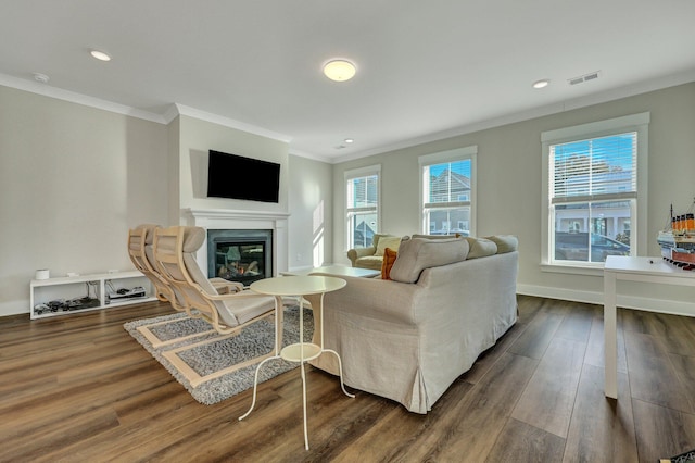 living area with dark wood-type flooring, a glass covered fireplace, visible vents, and crown molding