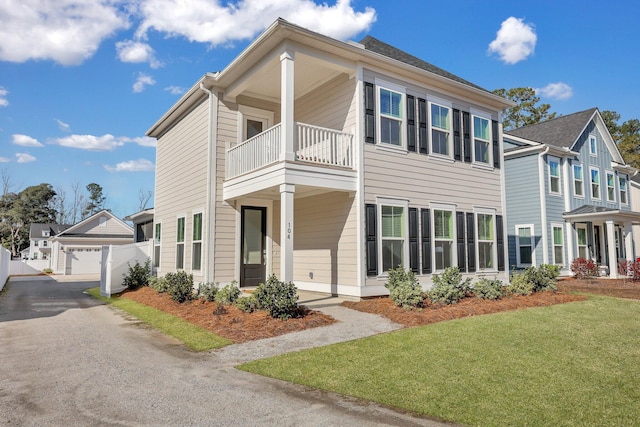 view of front of home with a balcony, a detached garage, fence, and a front lawn