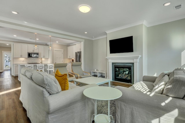 living room featuring recessed lighting, dark wood-style flooring, visible vents, ornamental molding, and a glass covered fireplace