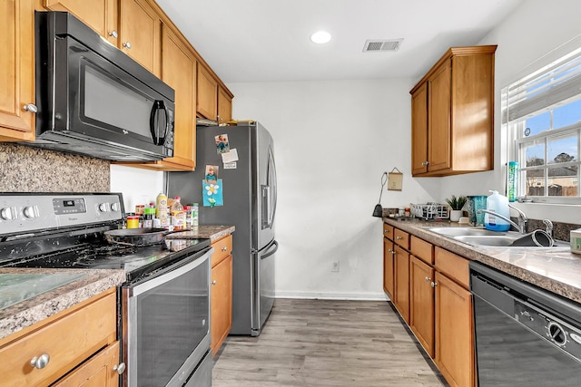 kitchen with brown cabinetry, black appliances, visible vents, and light wood-style flooring