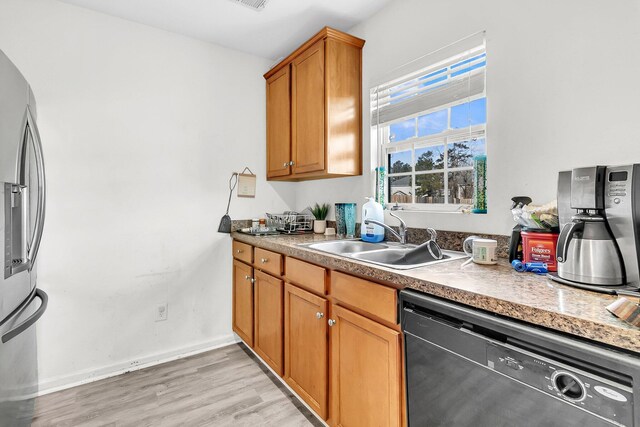 kitchen with a sink, stainless steel fridge, light wood-style floors, black dishwasher, and brown cabinetry