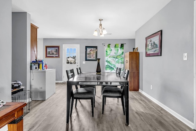 dining area with light wood-type flooring, visible vents, baseboards, and an inviting chandelier
