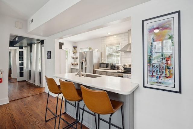 kitchen with a sink, tasteful backsplash, stainless steel appliances, a breakfast bar area, and wall chimney range hood