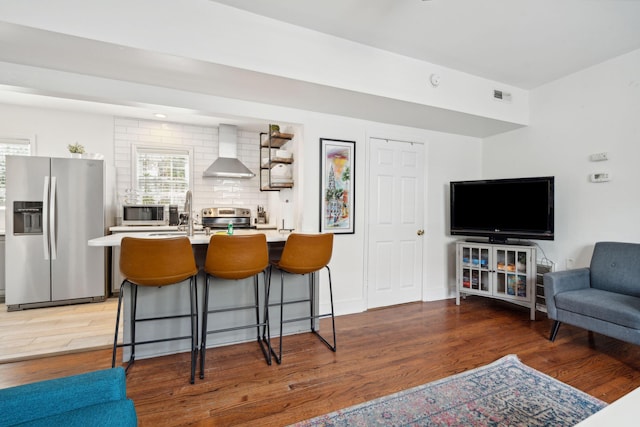 167 Coming St, Charleston, SC 29403 - kitchen with stainless steel appliances, wall chimney exhaust hood, light wood-style flooring, open floor plan, and a kitchen breakfast bar