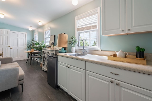 kitchen featuring dark tile patterned floors, lofted ceiling, stainless steel refrigerator, sink, and white cabinetry