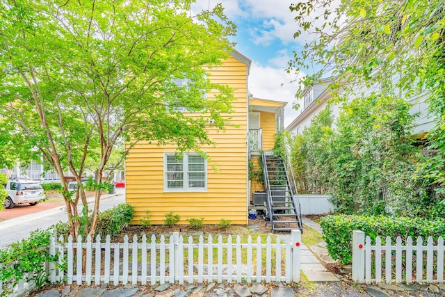 view of property hidden behind natural elements featuring a fenced front yard and stairs