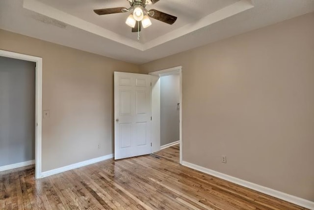 unfurnished bedroom with ceiling fan, light hardwood / wood-style flooring, and a raised ceiling