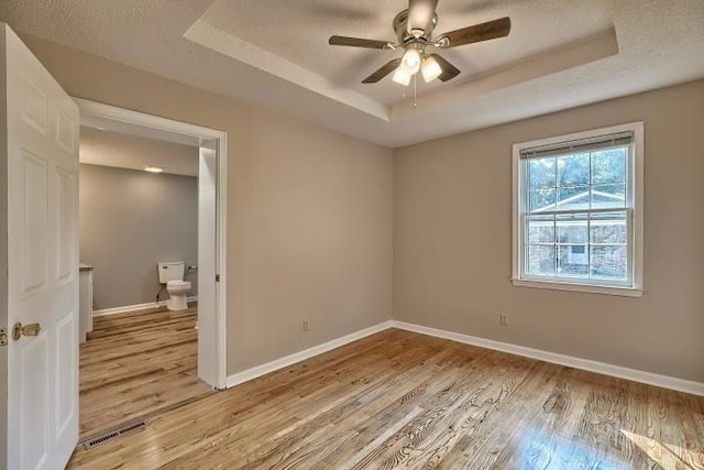 spare room featuring a raised ceiling, a textured ceiling, light wood-type flooring, and ceiling fan