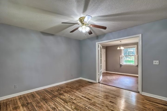 empty room with ceiling fan with notable chandelier, hardwood / wood-style floors, and a textured ceiling