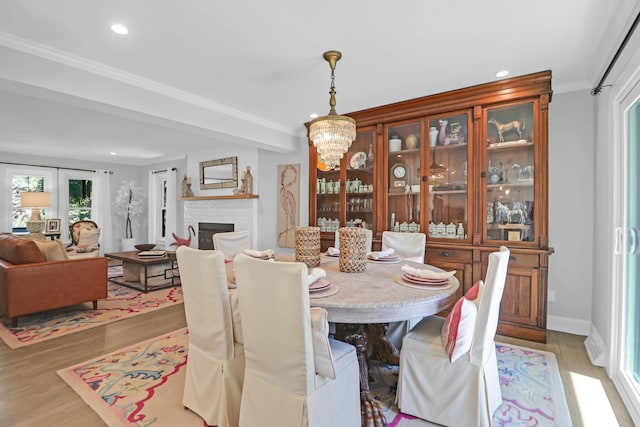 dining area with a notable chandelier, recessed lighting, ornamental molding, a brick fireplace, and light wood finished floors