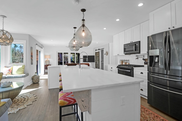 kitchen with a barn door, white cabinets, light countertops, black appliances, and a center island with sink