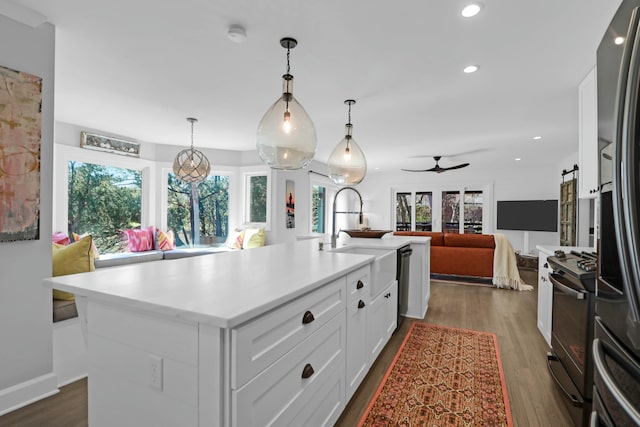 kitchen featuring pendant lighting, light countertops, a kitchen island with sink, a sink, and black appliances