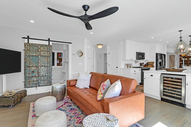 living area featuring recessed lighting, a barn door, ceiling fan, wood finished floors, and beverage cooler