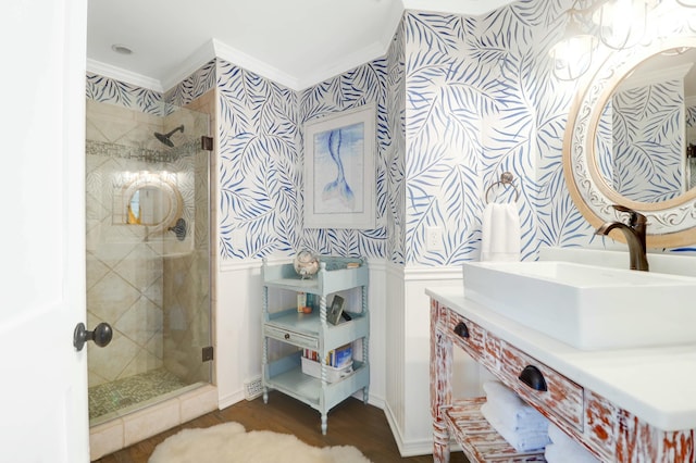 bathroom with wallpapered walls, ornamental molding, wood finished floors, vanity, and a shower stall