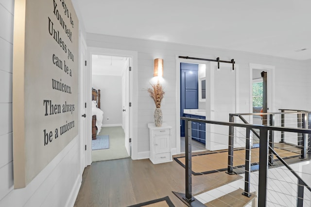 hall featuring baseboards, a barn door, attic access, and wood finished floors