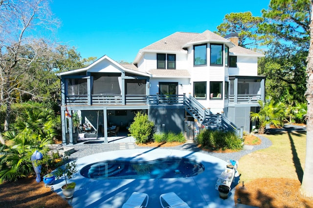 back of house featuring a patio, a shingled roof, a sunroom, stairs, and a chimney