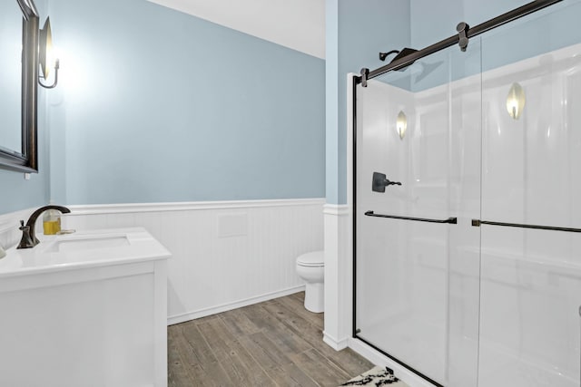 bathroom featuring a wainscoted wall, toilet, a stall shower, a sink, and wood finished floors