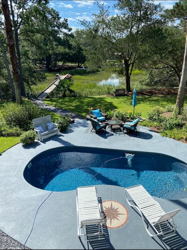 outdoor pool featuring a patio, a yard, an outdoor fire pit, and a water view