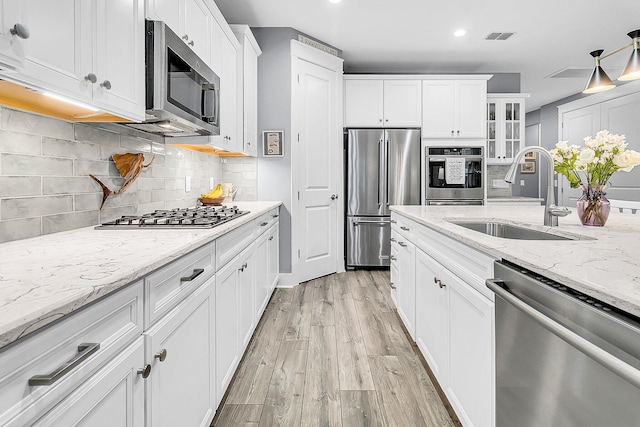 kitchen featuring appliances with stainless steel finishes, sink, backsplash, white cabinets, and light hardwood / wood-style floors