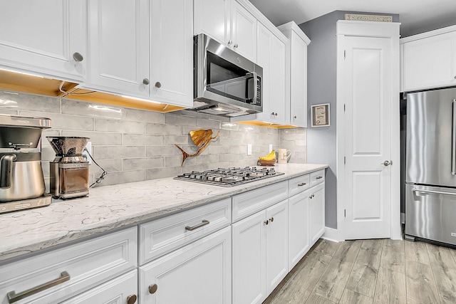 kitchen featuring appliances with stainless steel finishes, white cabinetry, backsplash, light stone counters, and light hardwood / wood-style flooring