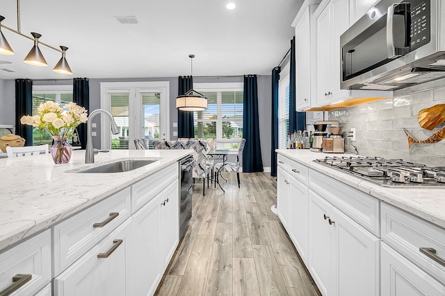 kitchen with appliances with stainless steel finishes, pendant lighting, sink, white cabinets, and light stone counters