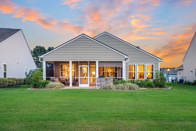 back house at dusk with a yard and a sunroom