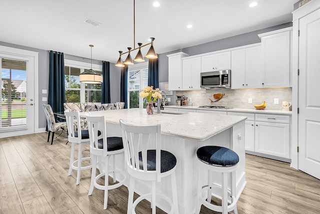 kitchen with stainless steel appliances, a kitchen island with sink, hanging light fixtures, and white cabinets