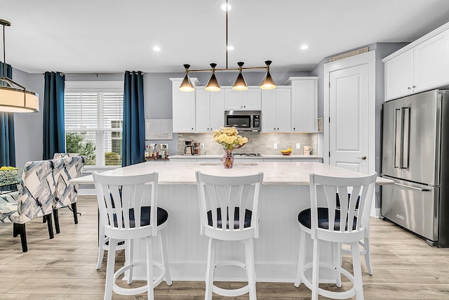 kitchen with pendant lighting, white cabinetry, stainless steel appliances, and a center island with sink