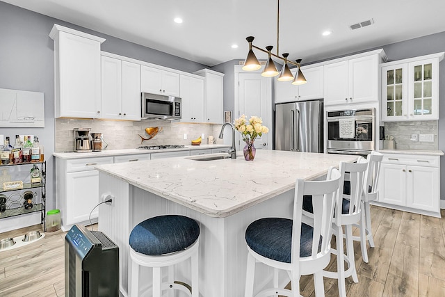 kitchen featuring sink, hanging light fixtures, light stone counters, stainless steel appliances, and a center island with sink