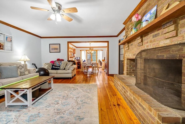 living area featuring ornamental molding, ceiling fan with notable chandelier, a fireplace, and hardwood / wood-style flooring