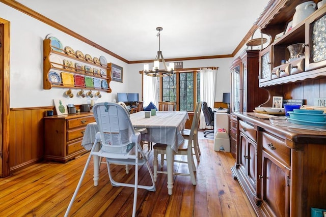 dining space featuring light wood-style floors, ornamental molding, wainscoting, wood walls, and a chandelier