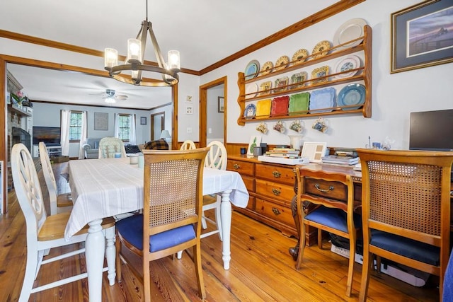 dining room with ceiling fan with notable chandelier, a fireplace, crown molding, and wood finished floors