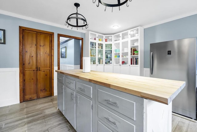 kitchen featuring a wainscoted wall, wood counters, freestanding refrigerator, crown molding, and wood finish floors