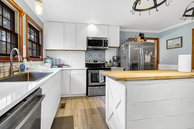 kitchen featuring a sink, appliances with stainless steel finishes, backsplash, light wood finished floors, and crown molding