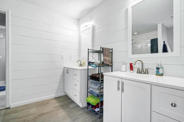 full bath with wood walls, wood finished floors, two vanities, a sink, and baseboards