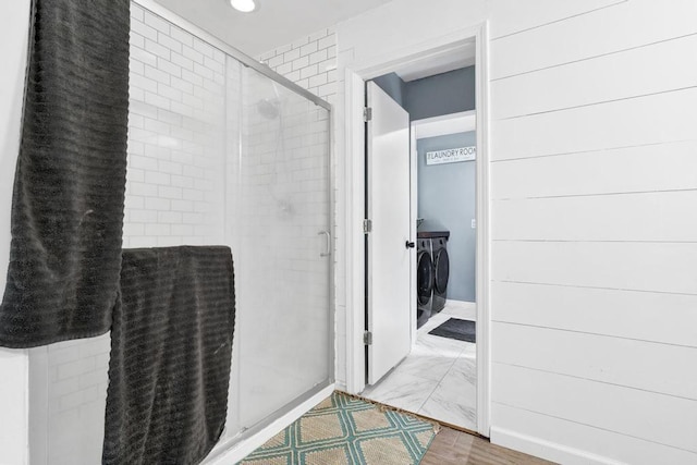 bathroom featuring marble finish floor, separate washer and dryer, a stall shower, and baseboards