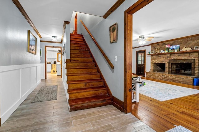 stairway with a decorative wall, a fireplace, a ceiling fan, ornamental molding, and wood tiled floor