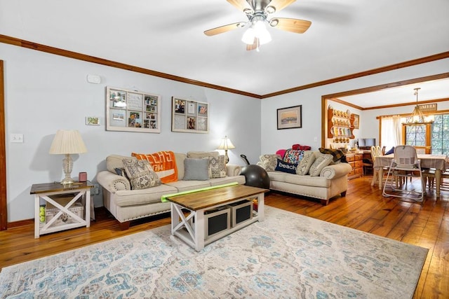 living room with ceiling fan with notable chandelier, hardwood / wood-style floors, baseboards, and crown molding