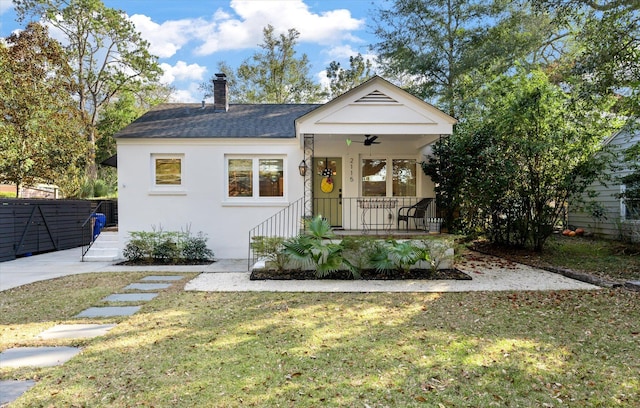 view of front of house featuring a ceiling fan, a porch, a chimney, stucco siding, and a front lawn