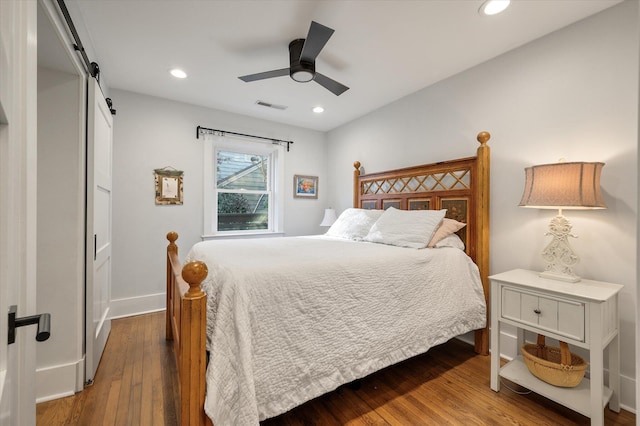 bedroom with hardwood / wood-style floors, visible vents, baseboards, recessed lighting, and a barn door