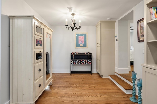 hallway featuring a chandelier, visible vents, light wood-type flooring, and baseboards