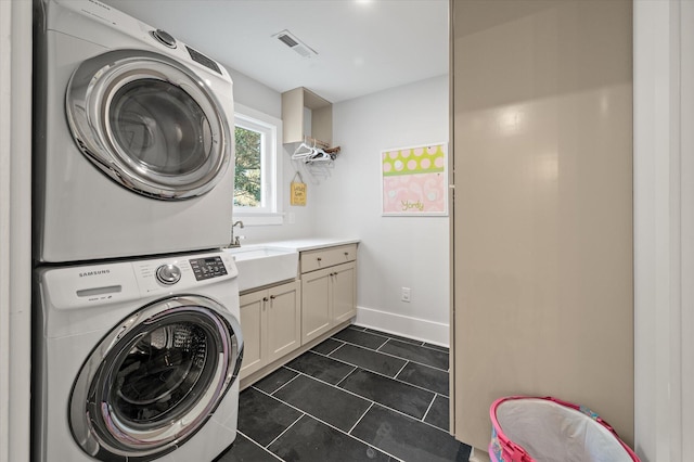 laundry room featuring stacked washer / dryer, visible vents, dark tile patterned floors, cabinet space, and a sink